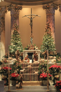 Poinsetta flowers, colorful fabrics, and nativity sculptures decorate the alter of a church.