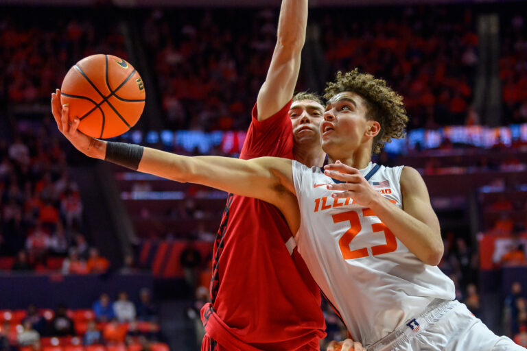 Illinois basketball player with out stretched arm being defended by a Wisconsin basketball player.