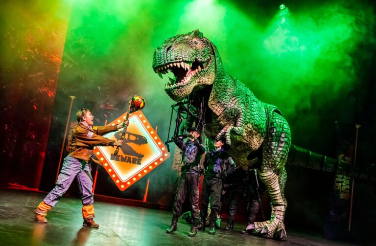 A person holds a stick-like object toward a large dinosaur puppet.