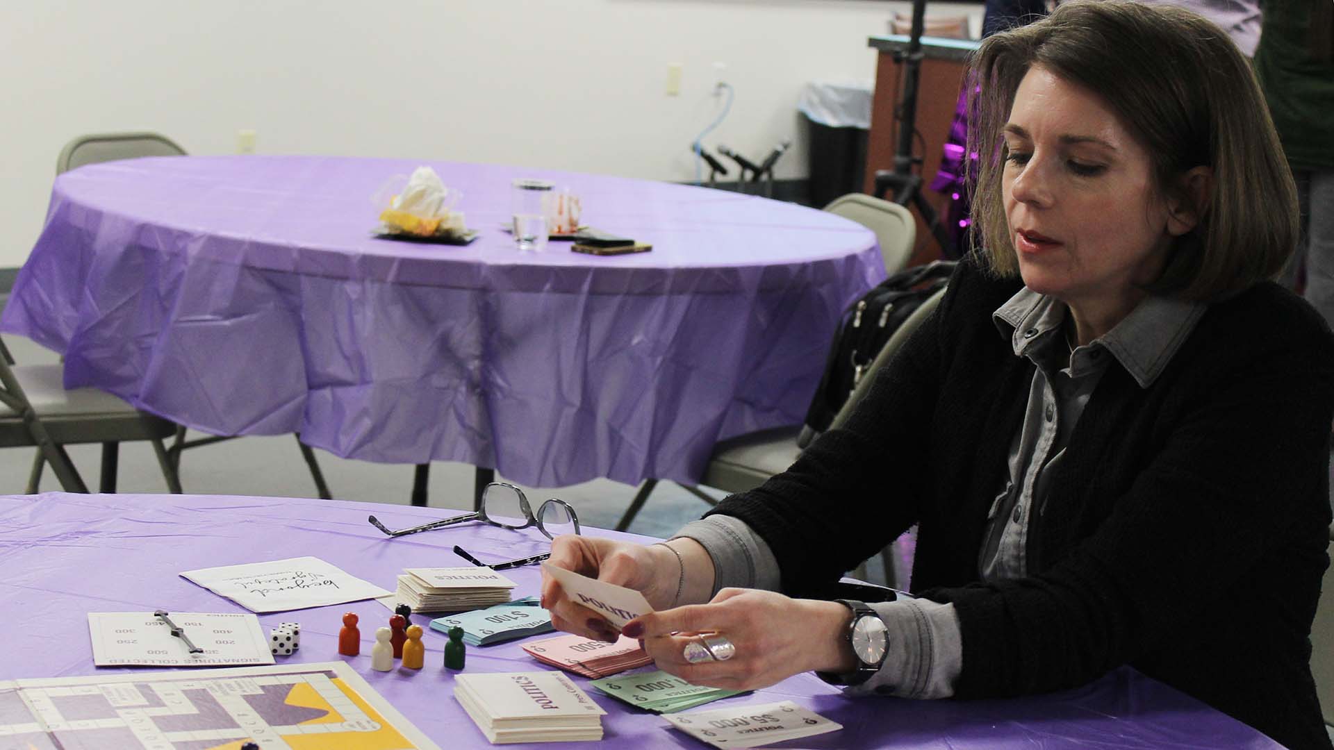 A white woman plays a board game on a purple tablecloth.