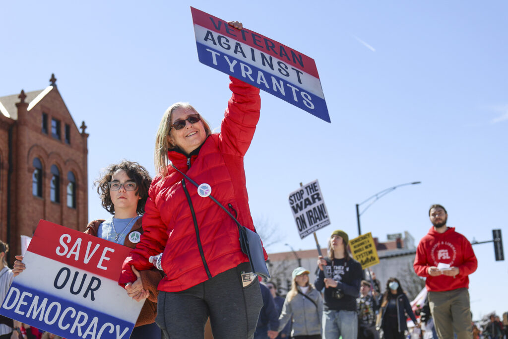 People carry signs saying "Save our democracy" and "Veterans against tyrants"
