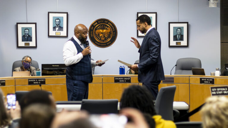 Urbana Mayor DeShawn Williams holds a paper and a microphone. Standing next to him, Verdell Jones III raises his right hand.