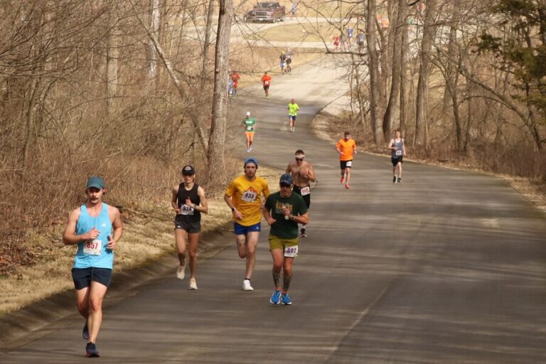 A group of runners jog up a hill surrounded by trees