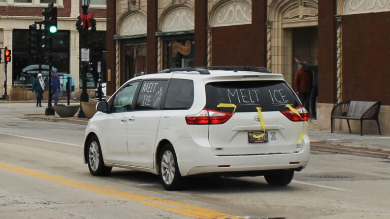 A white SUV in Urbana's downtown is decorated with yellow streamers and writing that says, "Melt ICE" and "ICE out for Good." The car was part of a caravan in January 2026 protesting the killing of Renee Good by Immigration and Customs Enforcement.