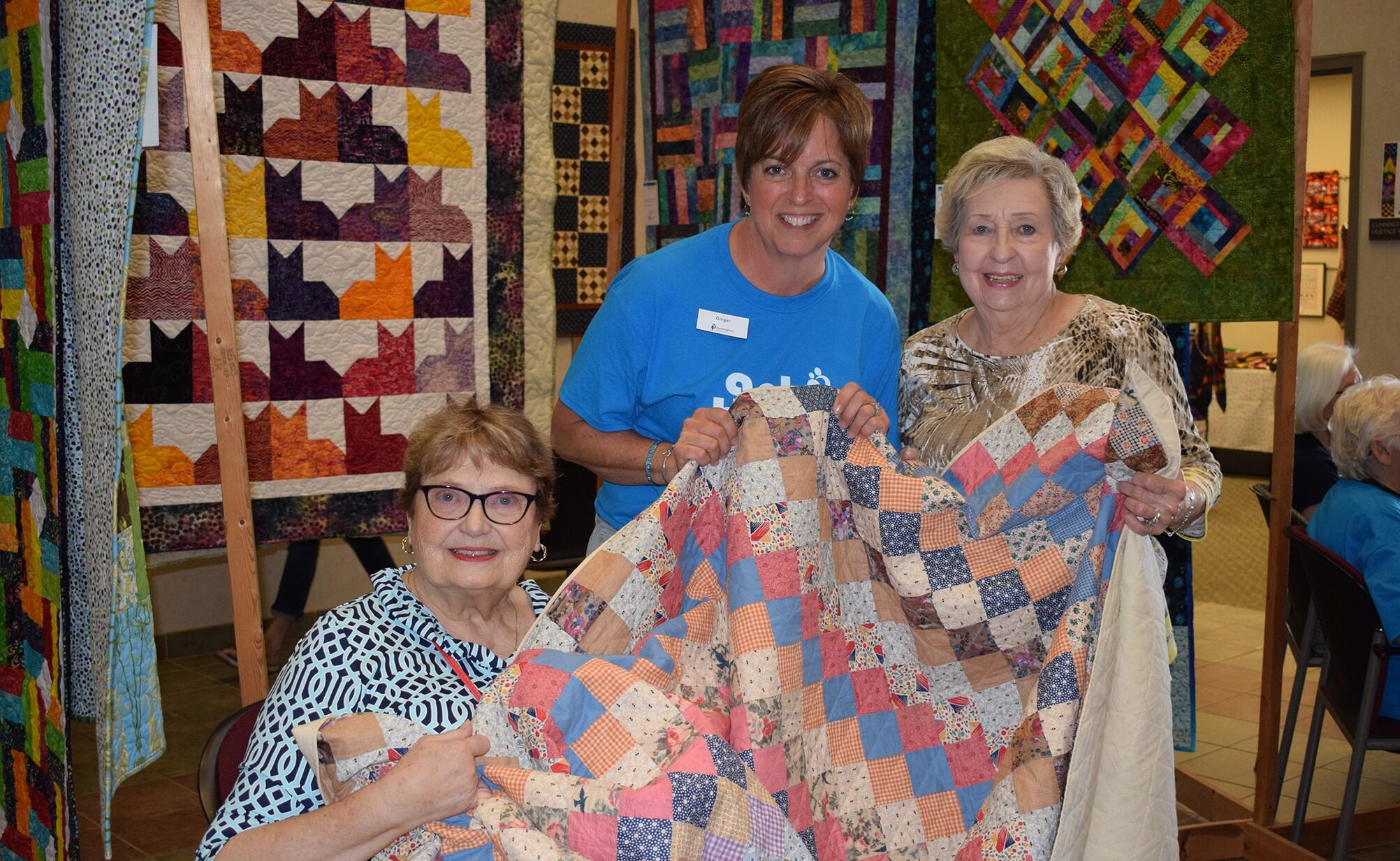 Three women pose while holding a quilt.