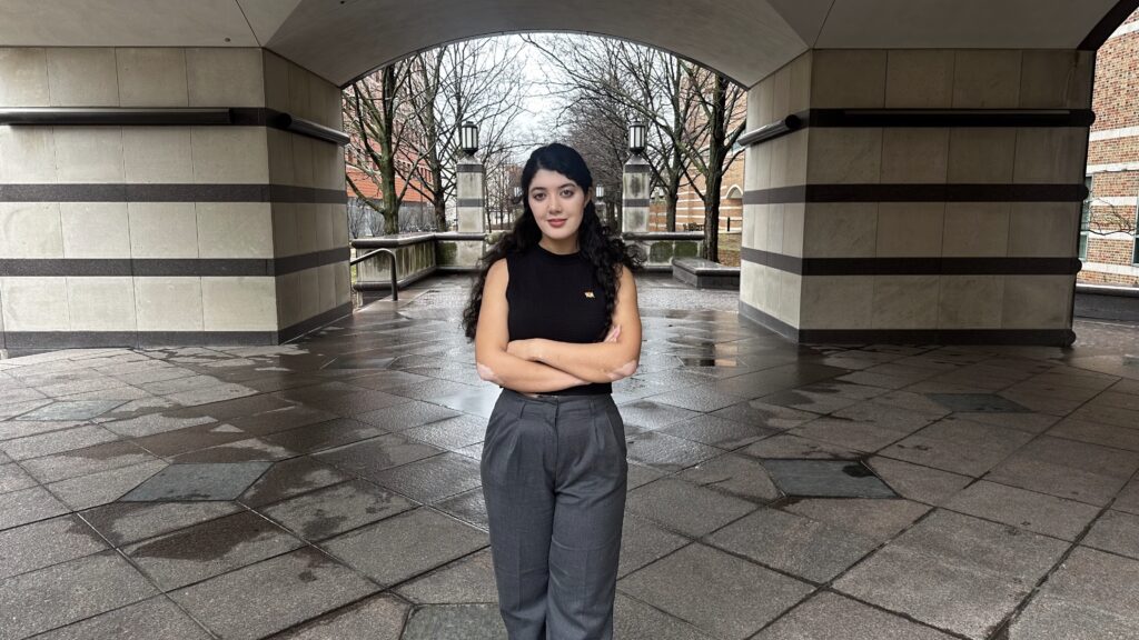 A woman stands with her arms crossed under an arch.