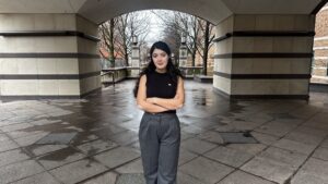 A woman stands with her arms crossed under an arch.