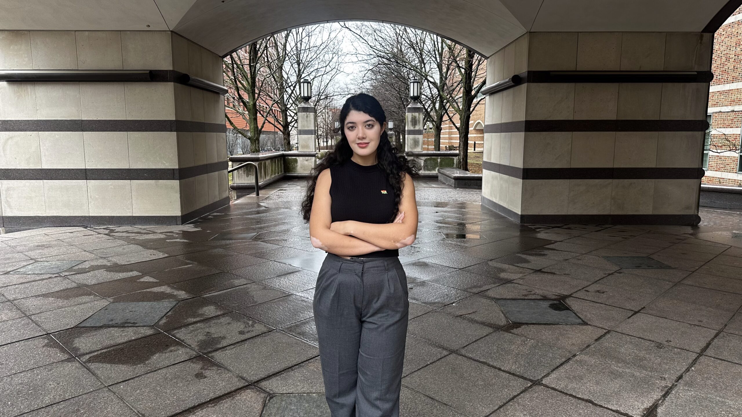 A woman stands with her arms crossed under an arch.