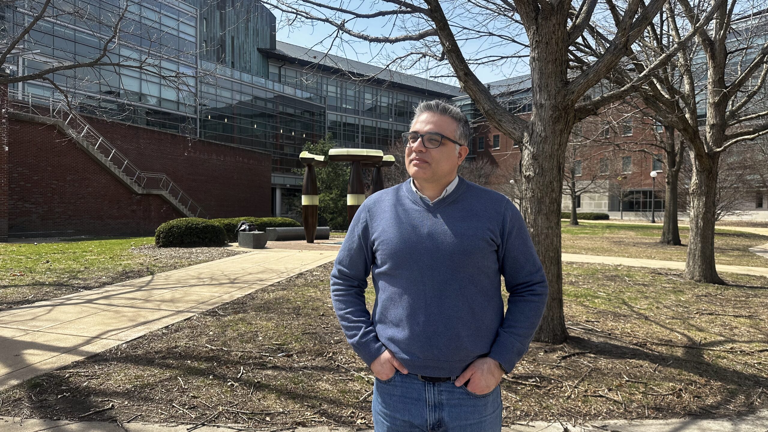 A man stands in an outdoor courtyard with his hands at his hips.