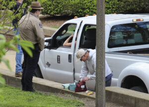 A man digs in a small bag while he and a few others stand around a work truck.