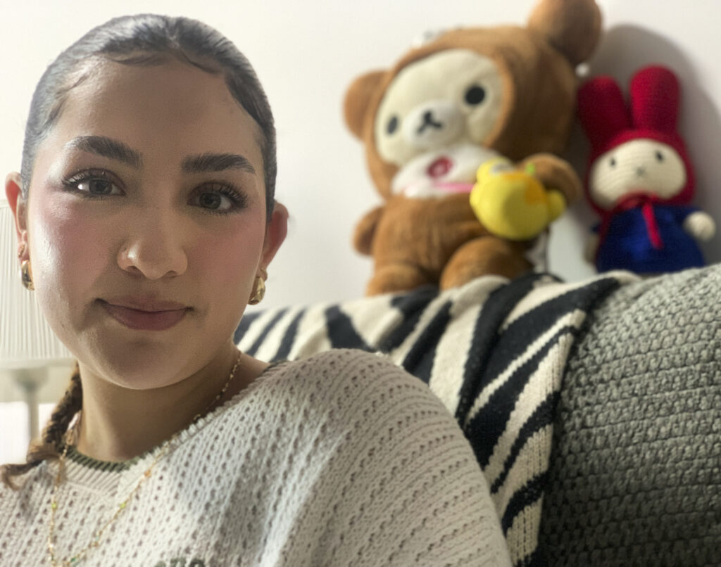 A woman poses for a photo. Stuffed animals are on the couch behind her.