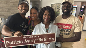 A woman and her three adult children stand and smile at the camera, holding a brown street sign that reads "Honorary Patricia Avery-Neal Way."