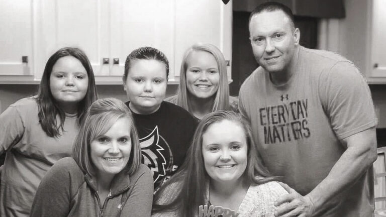 A black and white photo of a family standing in a kitchen.