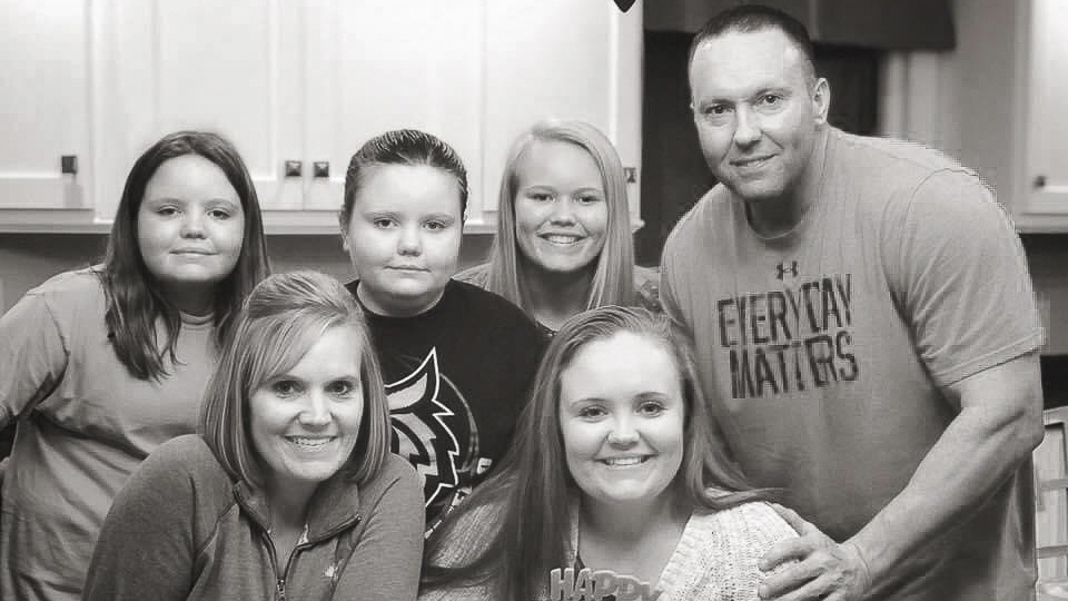 A black and white photo of a family standing in a kitchen.