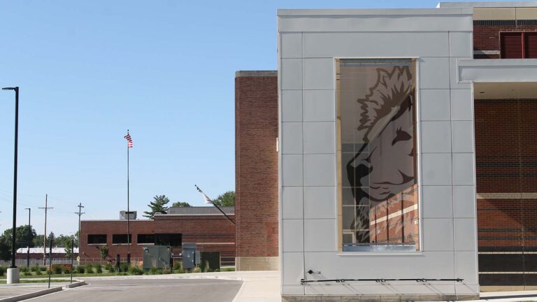 A large transparent screen with an outline of a lion fills a partially open wall at the end of a large school building.