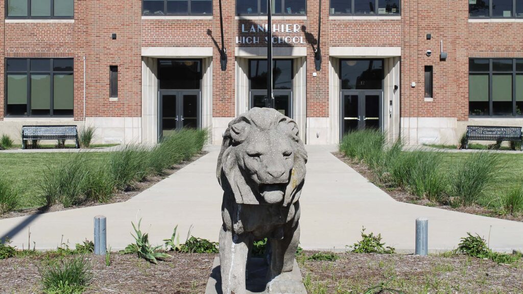 A lion sculpture is in the foreground with a flagpole and white lettering "Lanphier High School" on a brick school building.