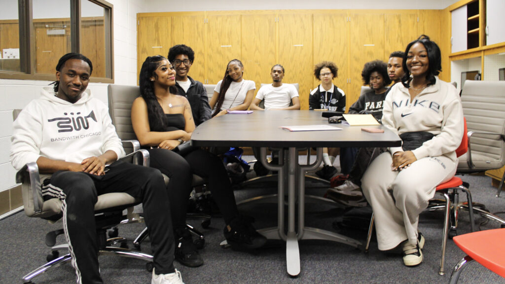 Nine Black students smile at the camera from around a table in a library conference room.