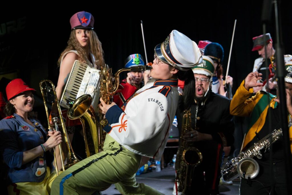Performers play instruments in marching band inspired outfits.