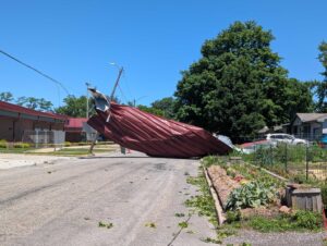 A piece of a red metal roof is in the middle of the road and dragging down a power line. 