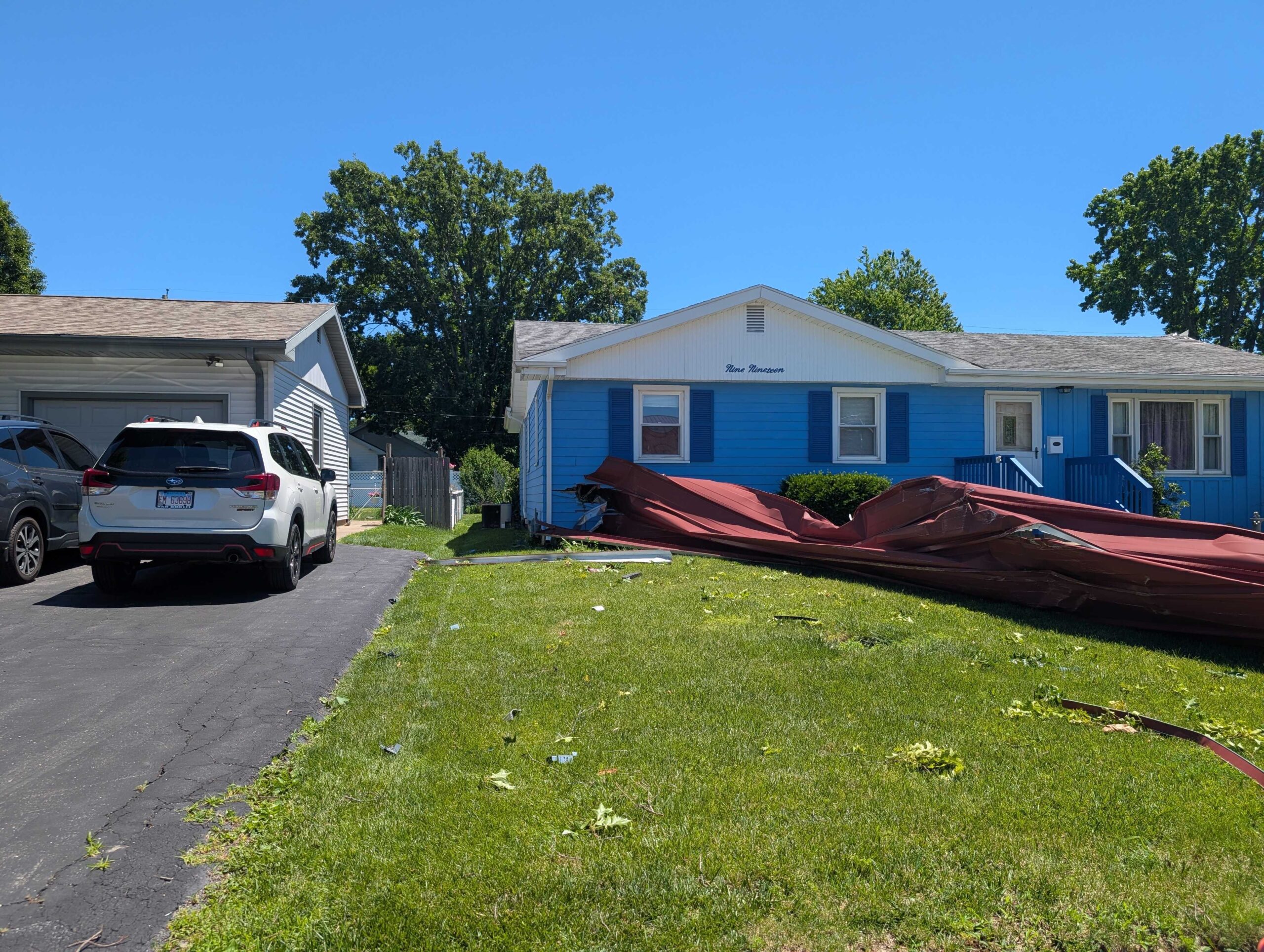 A piece of a red metal roof punctures a blue house.