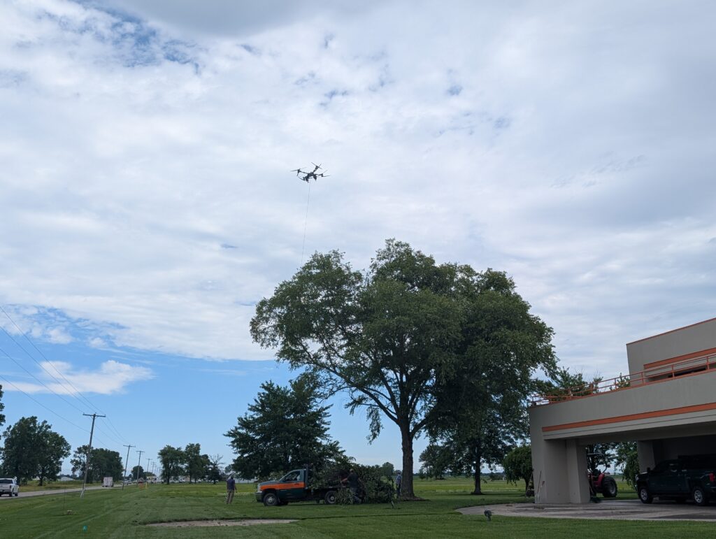 A drone flies above a tree and a pickup truck filled with branches.