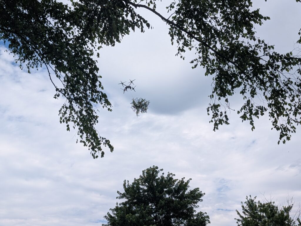 A drone flies up carrying a bundle of branches.
