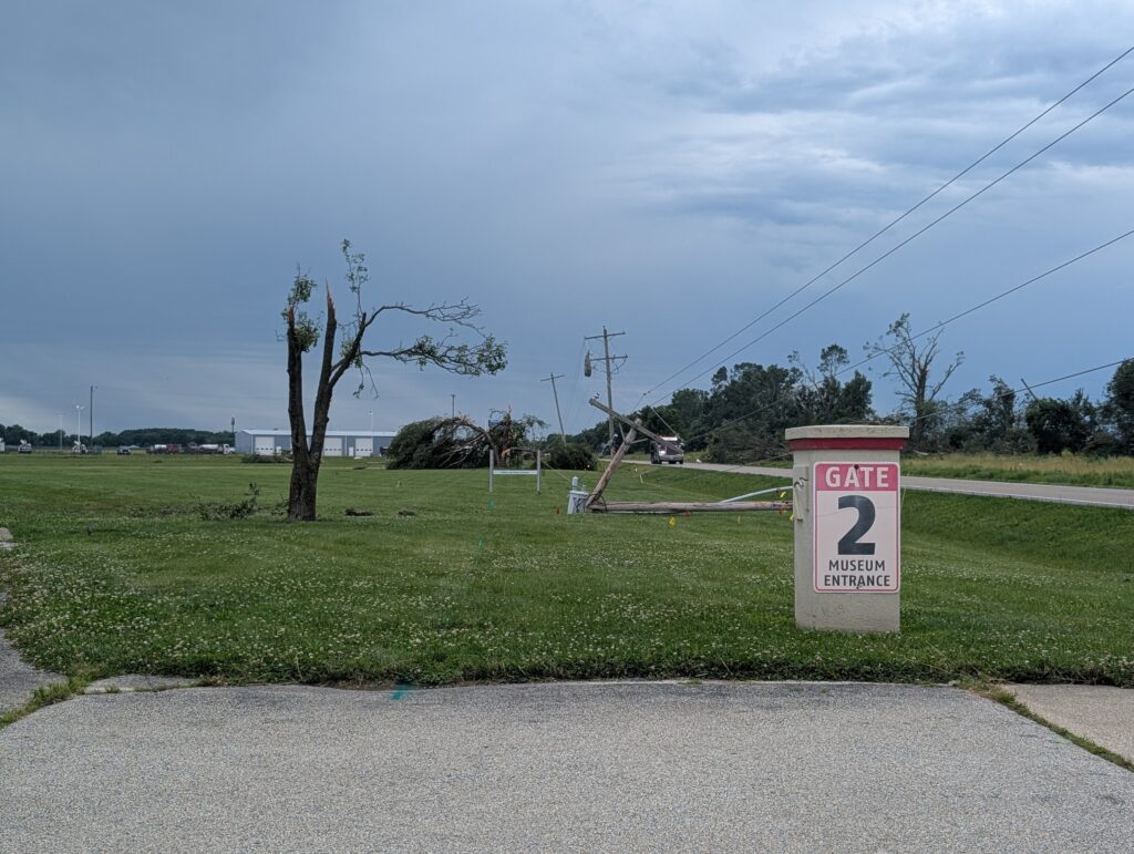 A pillar reads, "Gate 2 Museum Entrance." Behind it are damaged trees and a downed power line.