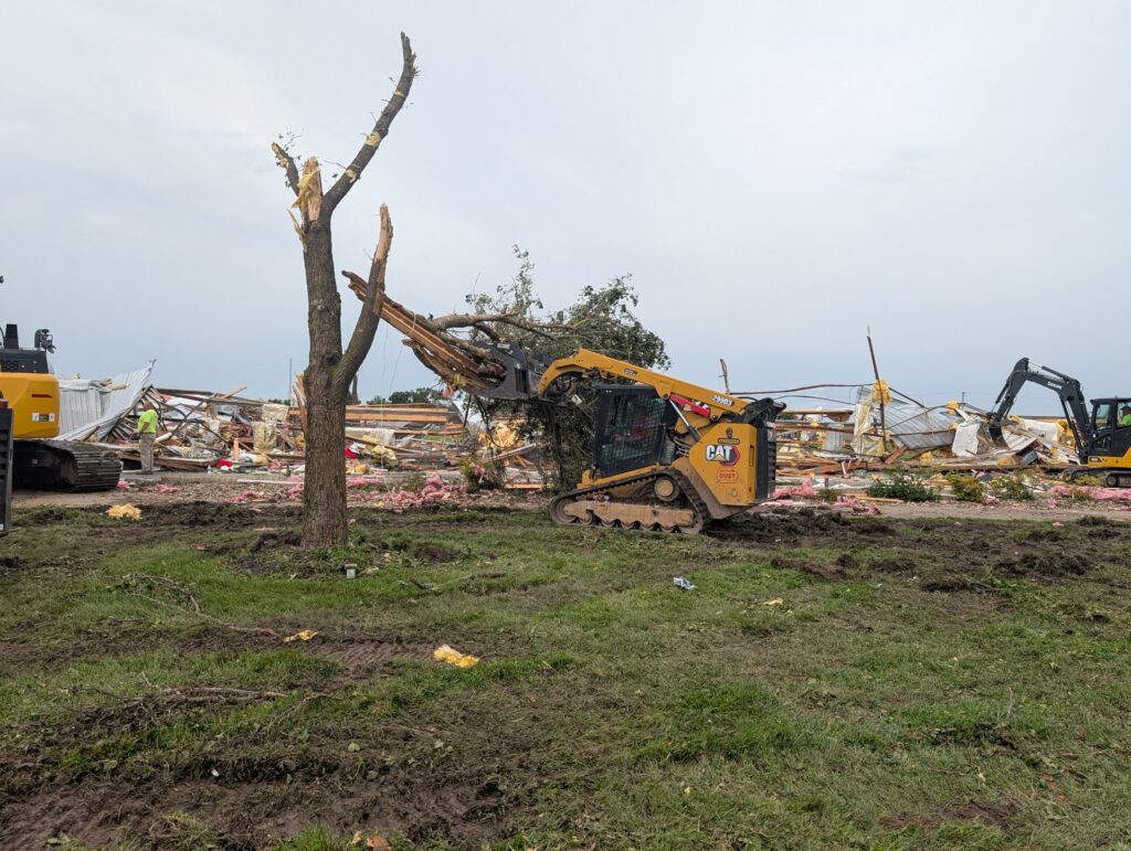 A piece of construction equipment removes part of a tree that had broken off.
