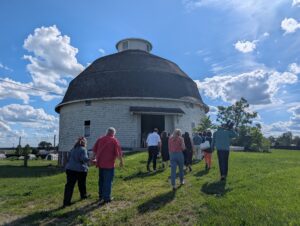 People walk through grass to a white round barn.