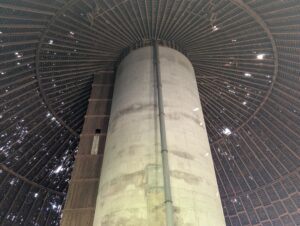 Looking up at a round roof with holes in it. A beam stands in the middle.