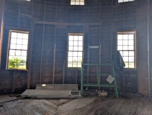 Three windows in a wooden barn. Pieces of wood lean against the wall.
