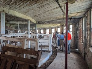 People walk around a circle of aged cow stalls.