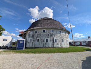 An aging white round barn with porta potties to the left.