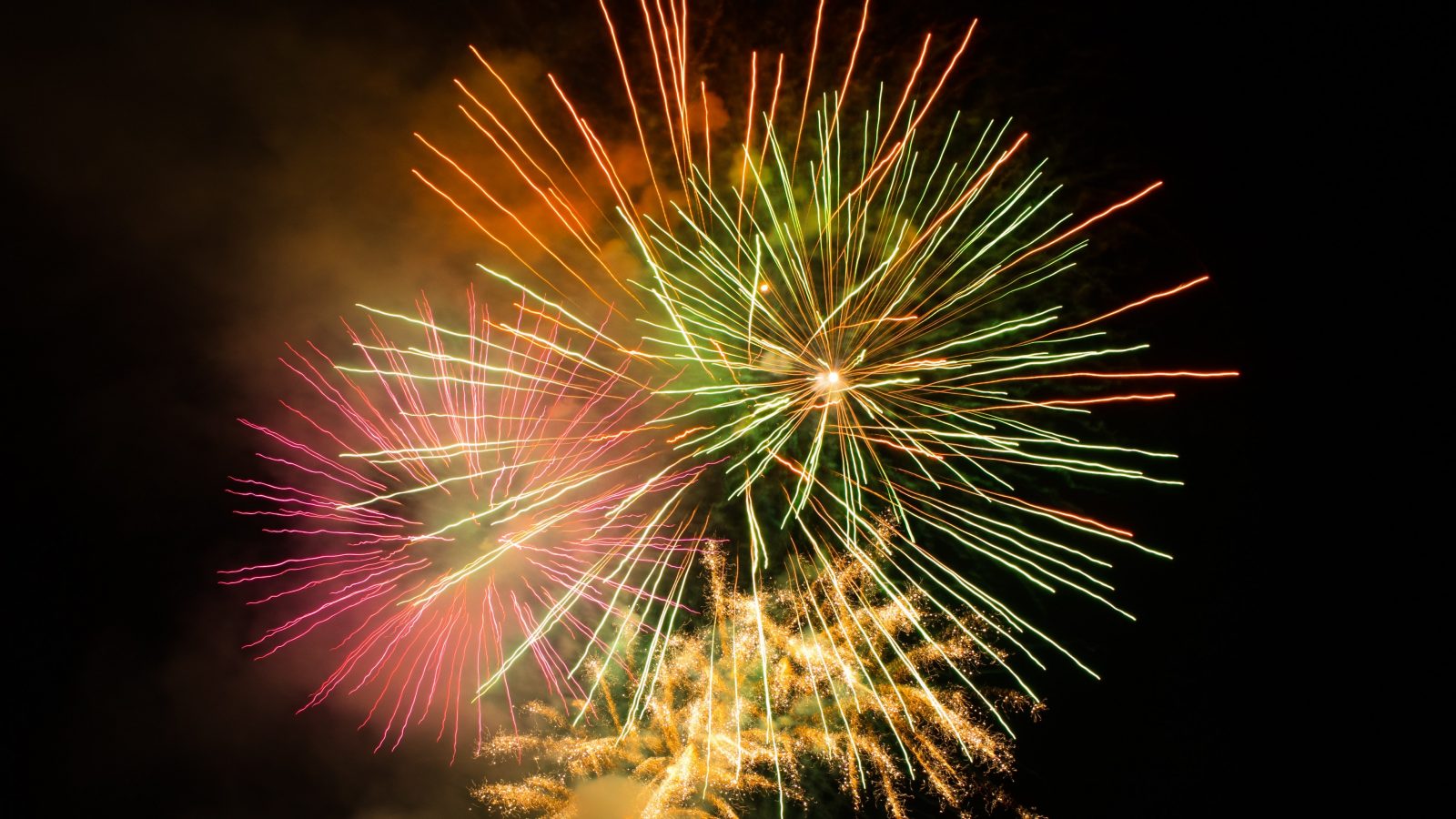 Multi-colored fireworks burst against a black sky.