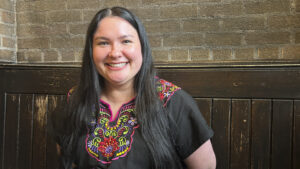 A woman with dark hair wearing a black blouse with a colorful pattern embroidered around the collar.