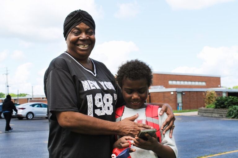 A grandmother and her adoptive son hug outside a school building.