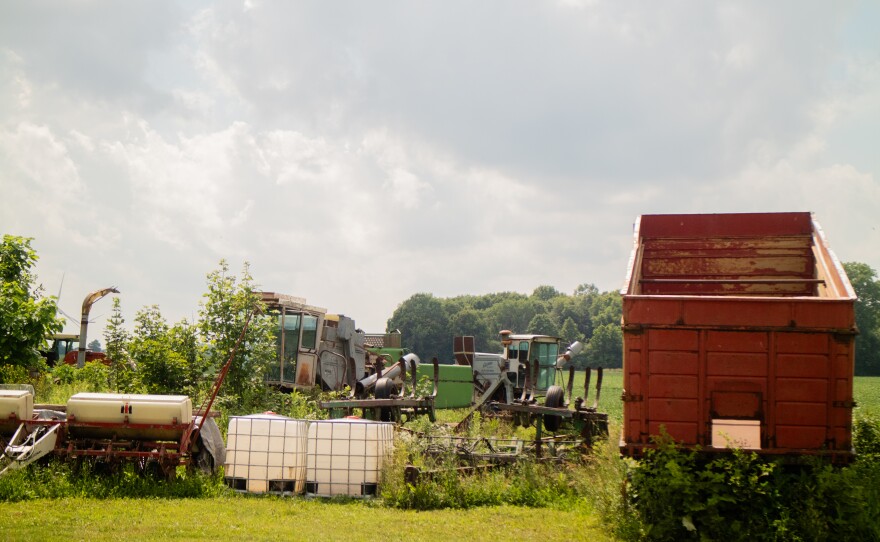 Old farm equipment surrounded by grass and weeds.