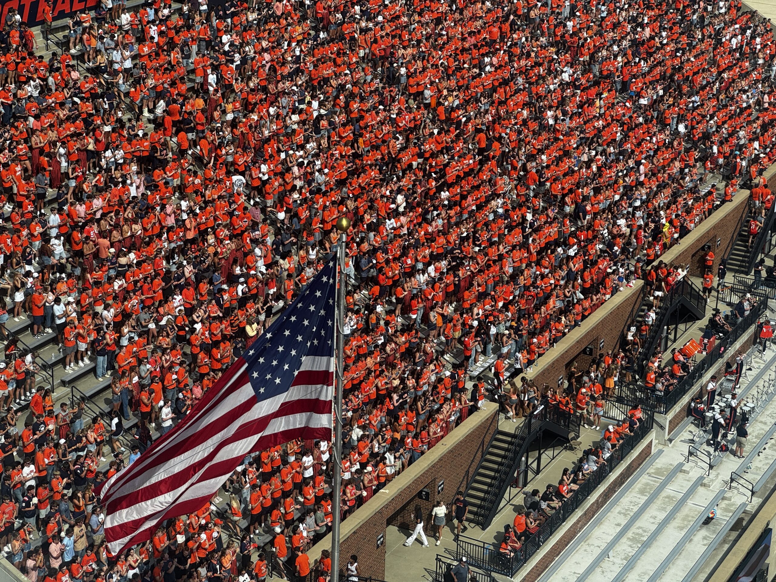 Illinois fans stand in the bleachers with an American flag hanging in front of them