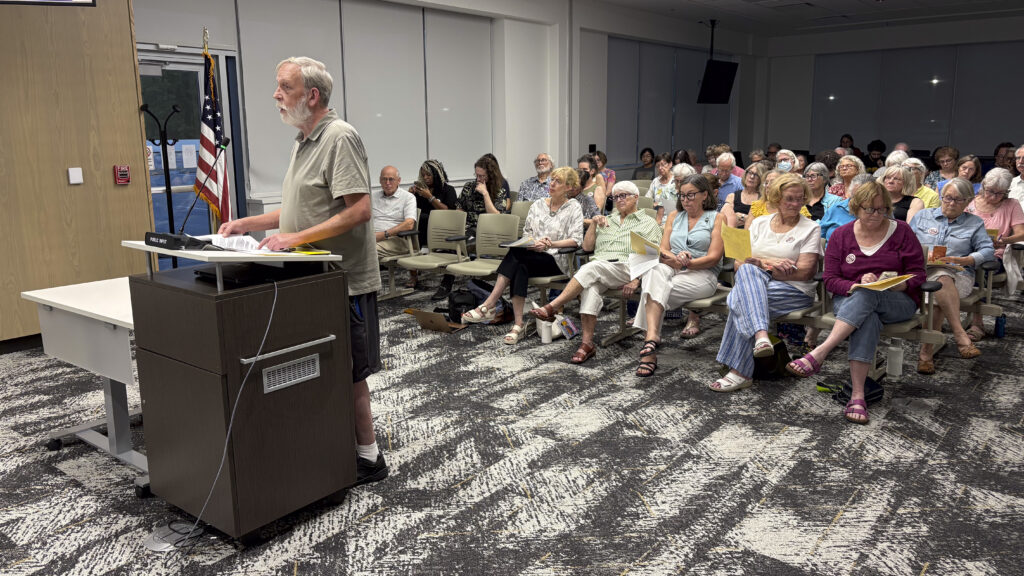 a man stands at a podium and a crowd of people are seated behind him