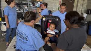 a child in a car seat and several adults gathered around