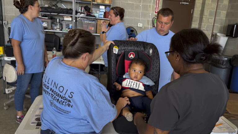 a child in a car seat and several adults gathered around