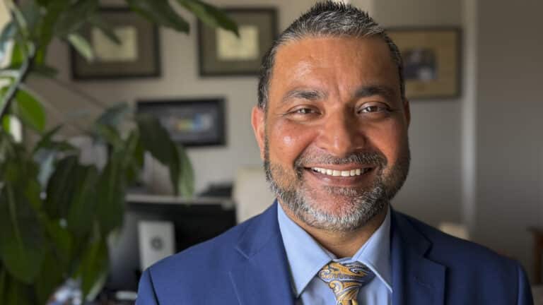a man in an office wearing a suit and tie and smiling