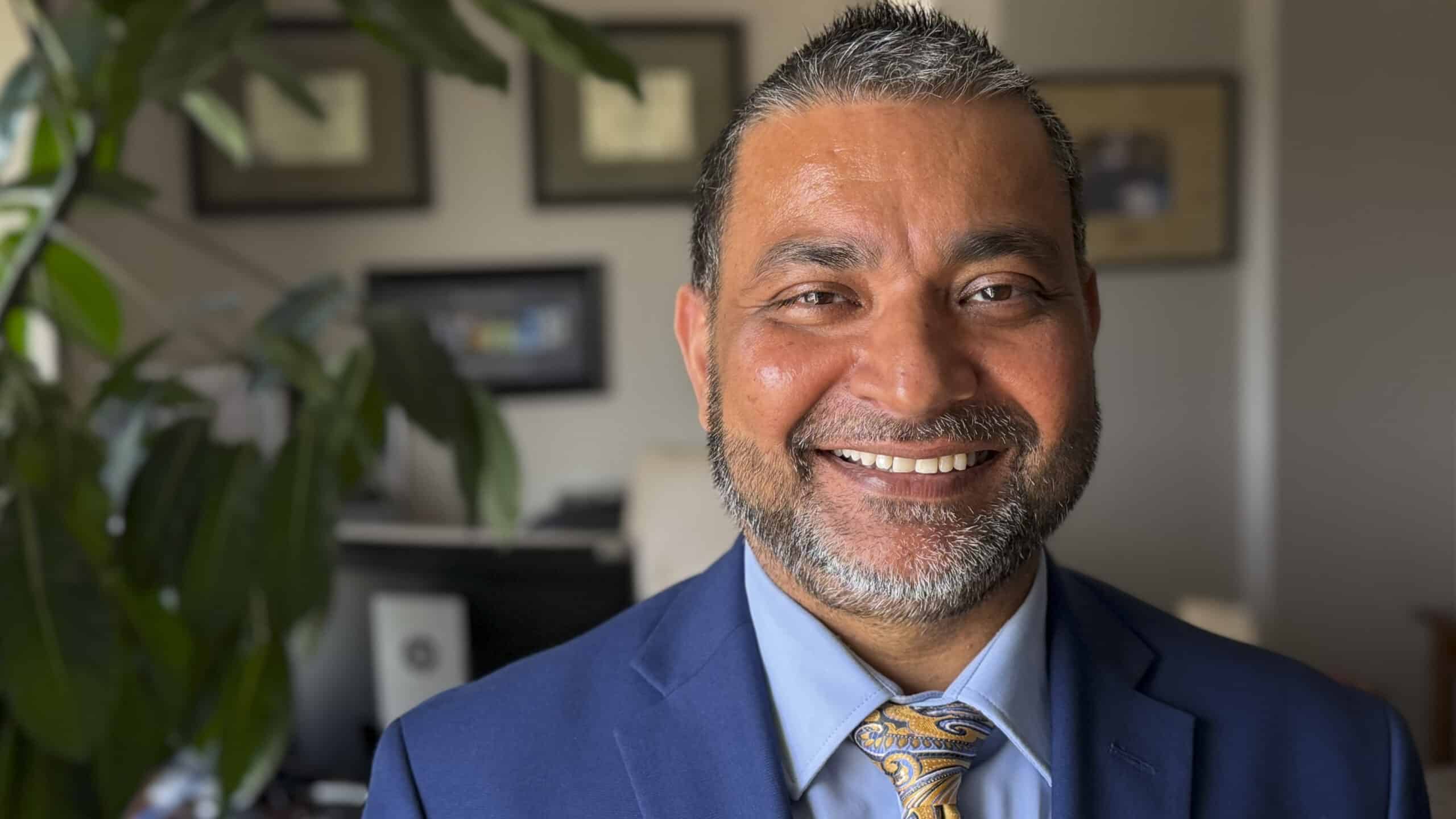 a man in an office wearing a suit and tie and smiling